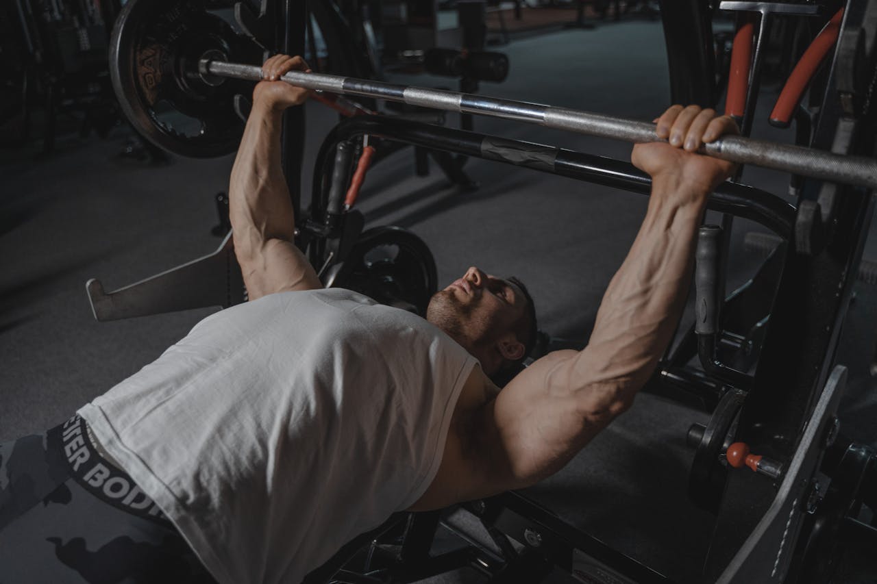 A focused man lifts heavy weights on a bench press machine in a dimly lit gym.